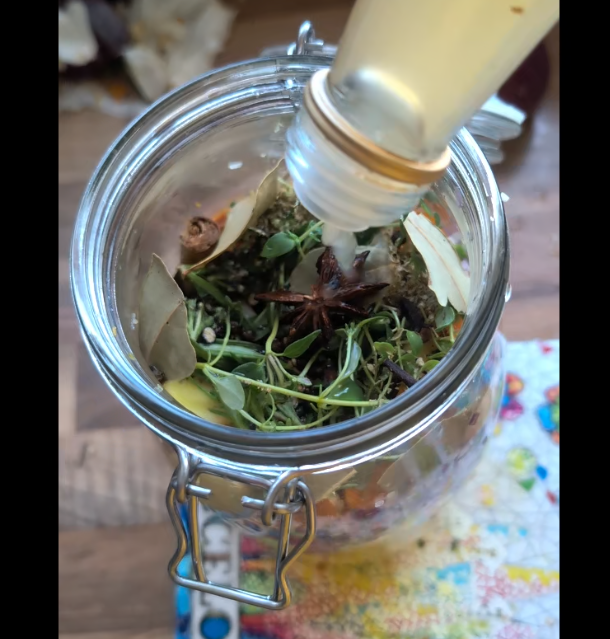 Frasco de vidrio con hierbas secas y especias, mientras se añade un líquido desde una botella.